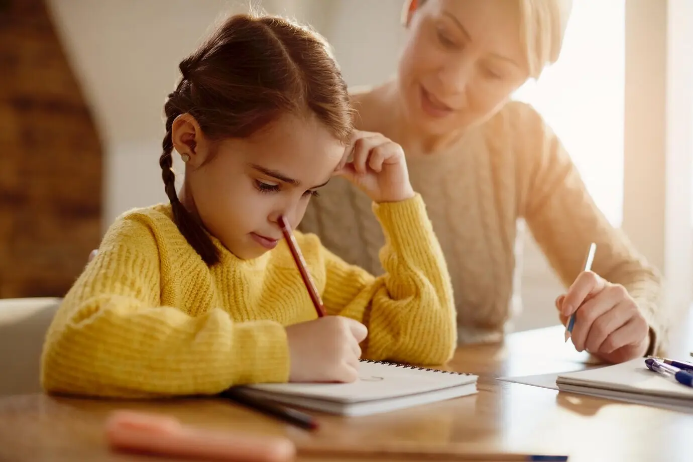 Niña pequeña adorable haciendo la tarea con la ayuda de su madre.